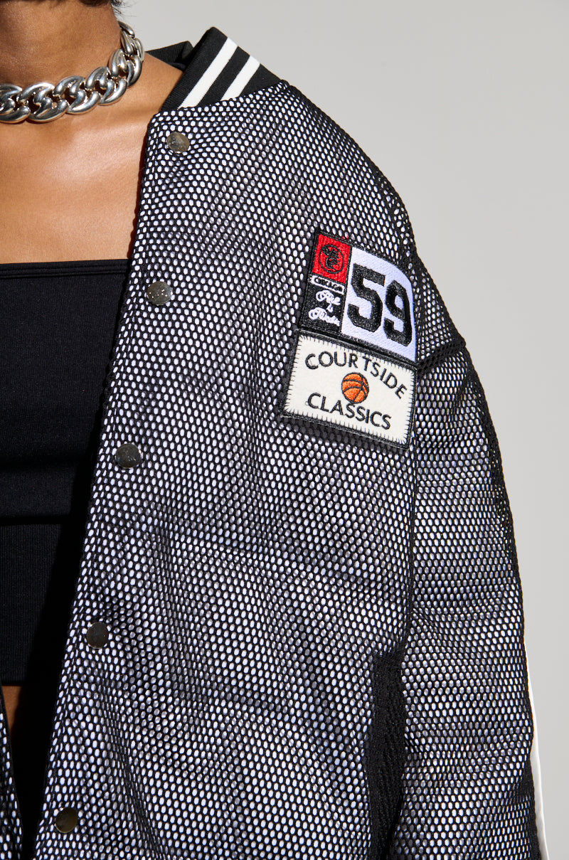 A person wearing the PLAYERS ONLY JERSEY BOMBER in textured black and white with metal buttons and athletic patches on the front. One of the patches reads "COURTSIDE CLASSICS" and includes a small basketball design. The image is cropped at the person's neck and wrist.