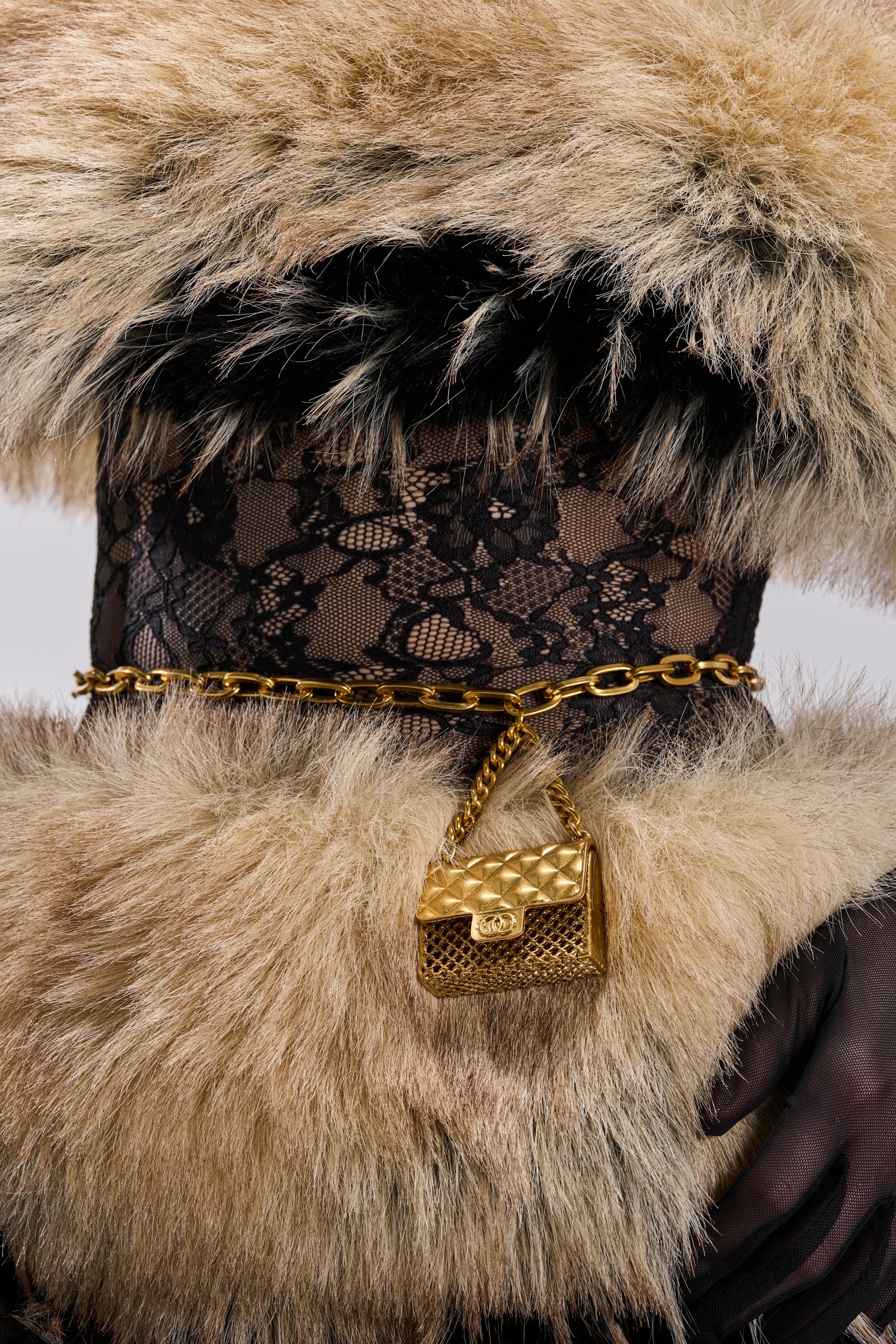 A person wearing a black lace scarf, a fur coat with a large fur collar, and the CALL ME COCO CHAIN BELT styled as a necklace with a quilted mini bag pendant. Only the neck and part of the chest are visible.