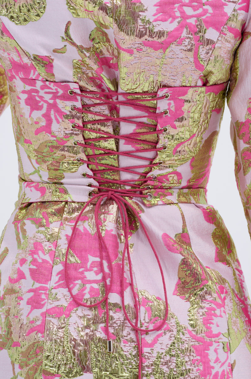 Close-up of the PRETTY IN PINK BROCADE BLAZER DRESS, showcasing pink and gold floral patterns with a metallic sheen, a crisscross lace-up corset detail, and a tied waist bow.