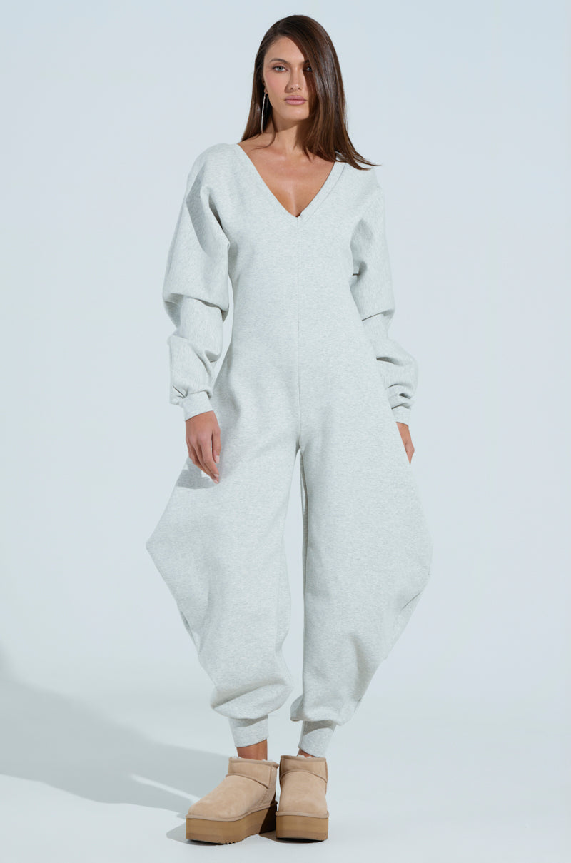 Someone in a light gray COMFY COZY SWEATSHIRT JUMPSUIT, featuring a plunging V-neck, voluminous sleeves, and wide balloon legs, pairs it with beige platform shoes on a plain white background.