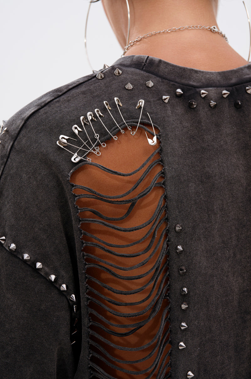 Close-up of a person wearing the MARGOT DISTRESSED STUDDED SHORT SLEEVE TEE with metal studs, a large ripped back section held by safety pins, and large hoop earrings.