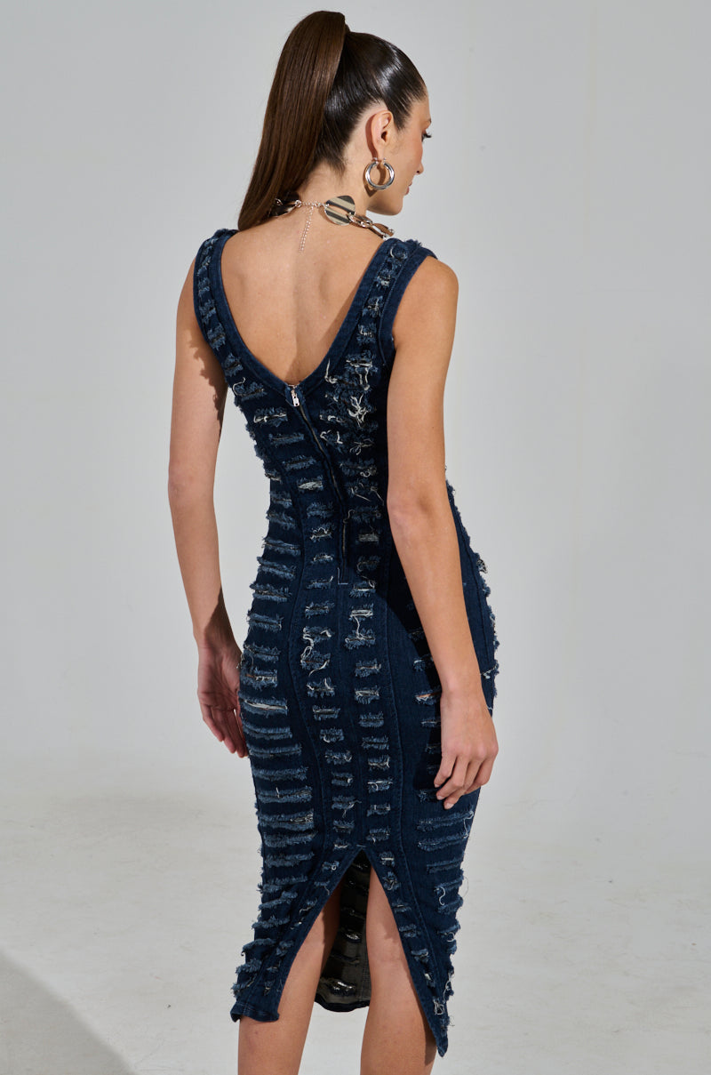 A woman with long hair in a ponytail wears the "She's Got It Shredded Denim Midi Dress in Dark Blue," showcasing its sleeveless, curve-hugging design, back zipper, V-shaped neckline, shredded details, and bottom slit. She accessorizes with hoop earrings and a chain necklace.