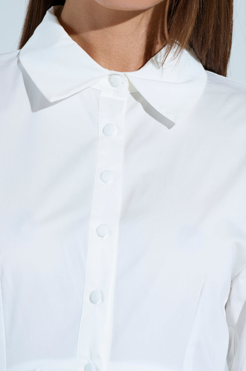 Close-up of a person wearing THE IT GIRL POPLIN MINI DRESS with its crisp, white button-up design and pointed collar. It features simple yet elegant clean lines, emphasizing the button-down front closures and fabric texture.