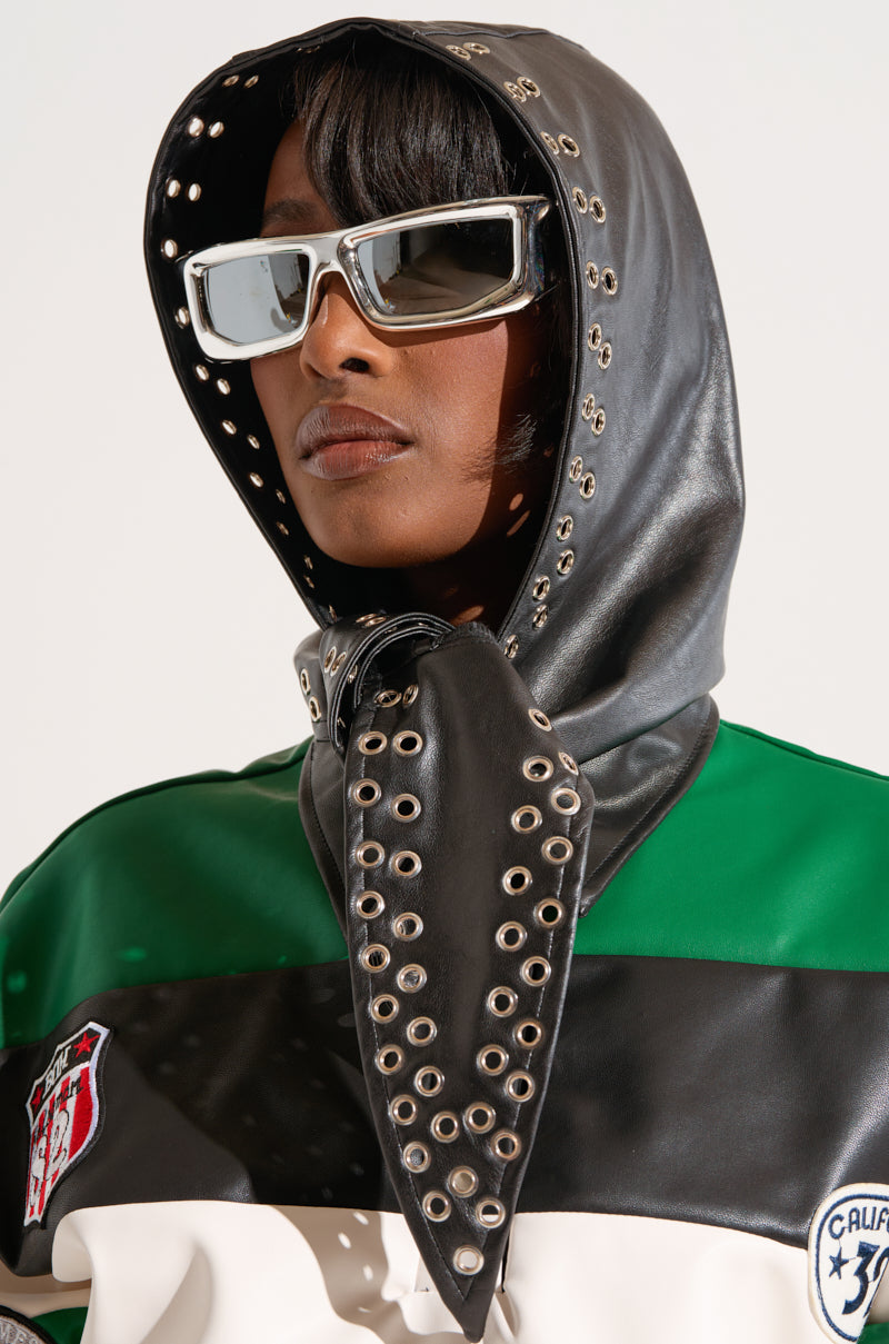 A person wearing the OH SO CHIC PU HEAD SCARF with black and green stripes, complete with metallic eyelets and an edgy design. Large reflective sunglasses obscure their neutral expression, while the hood is fastened with a knotted tie under the chin. The background is plain white.