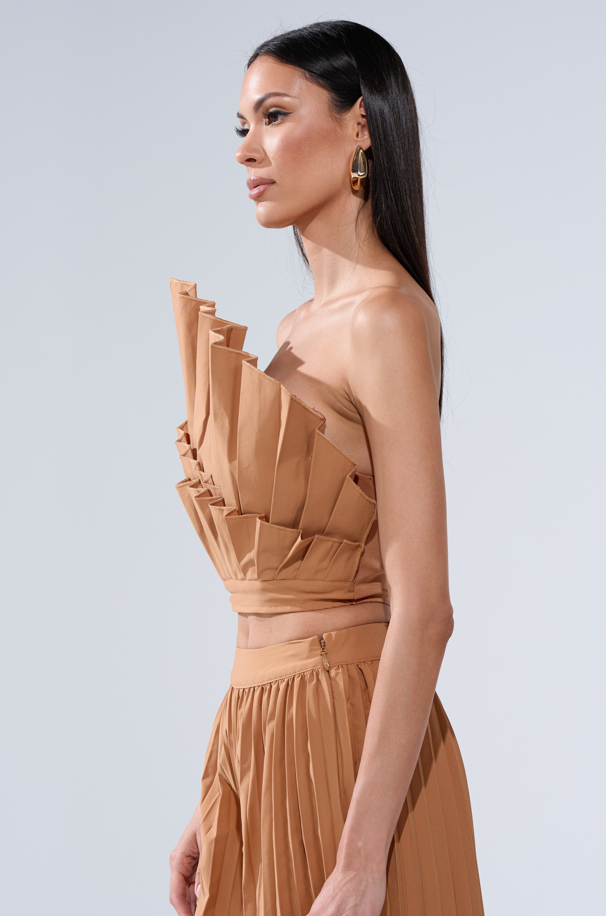 A woman with long dark hair wears the STAR OF THE NIGHT PLEATED BLOUSE and matching skirt, accessorized with gold hoop earrings, standing against a plain light gray background.