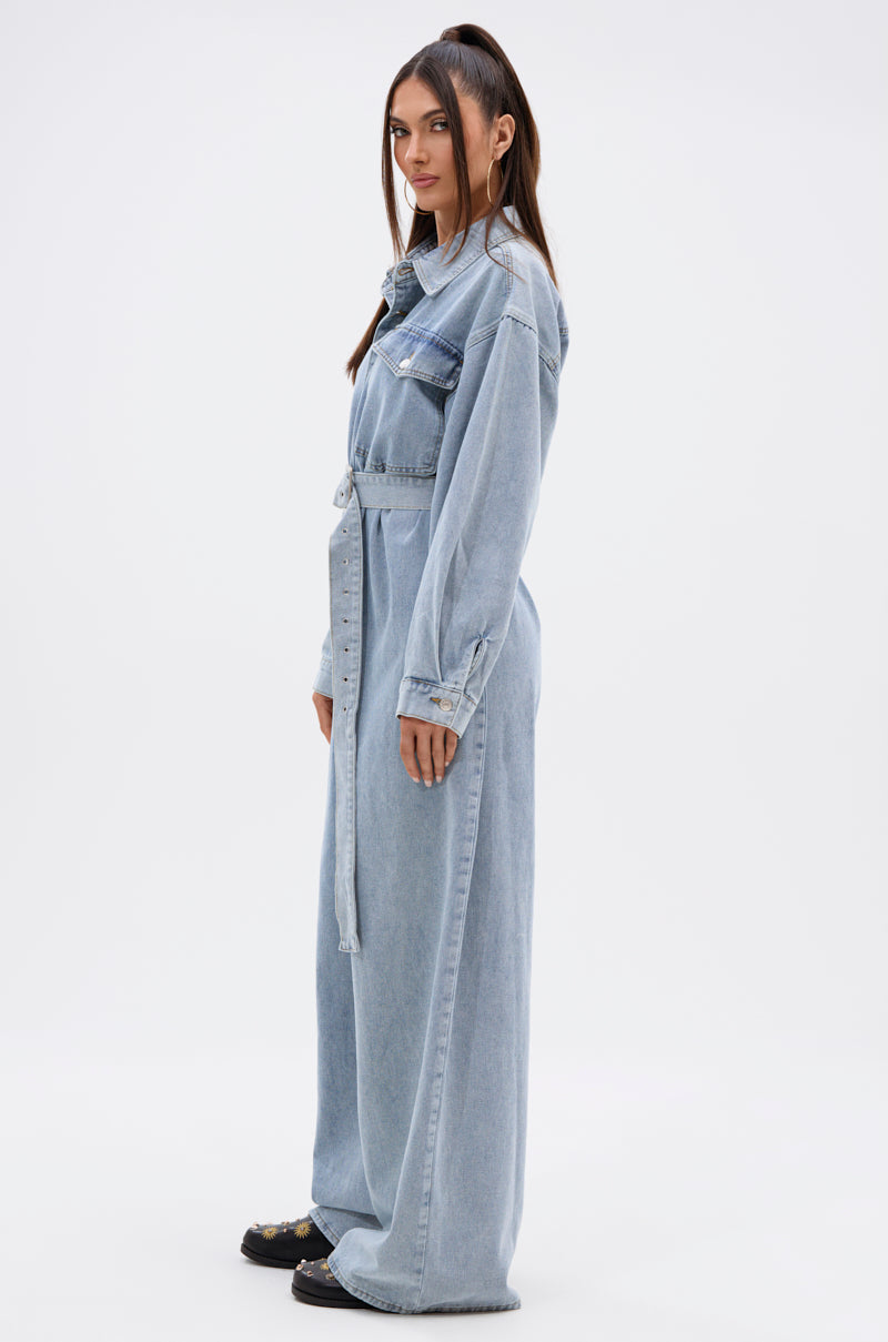 A woman in the NOT TODAY EXTREME OVERSIZED DENIM JUMPSUIT, with adjustable waist belt, long sleeves, and wide legs, stands sideways against a plain background. She has straight dark hair and looks slightly toward the camera.