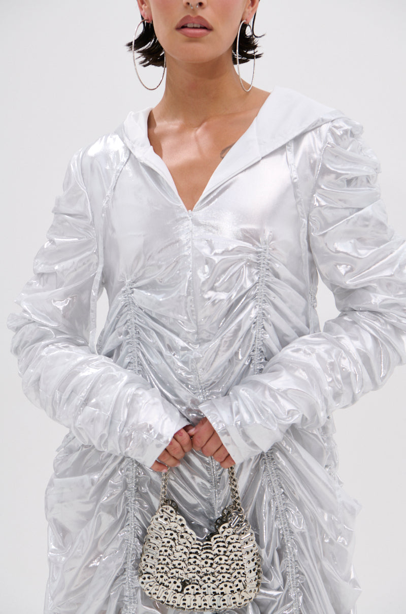 Wearing the WAYS TO GO METALLIC ADJUSTABLE DRESS IN WHITE, a person with large hoop earrings and dark hair holds a small chainmail handbag; only the lower half of their face is visible.