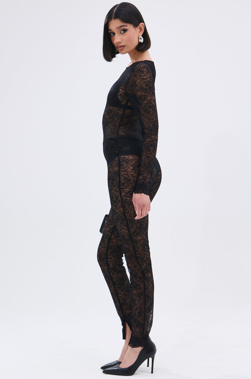 A woman with straight dark hair models the ONLY IF THERE'S BOTTLE SERVICE LACE JUMPSUIT, a curve-hugging floral lace piece, styled with black high heels and large round earrings. She poses in profile against a plain white background.