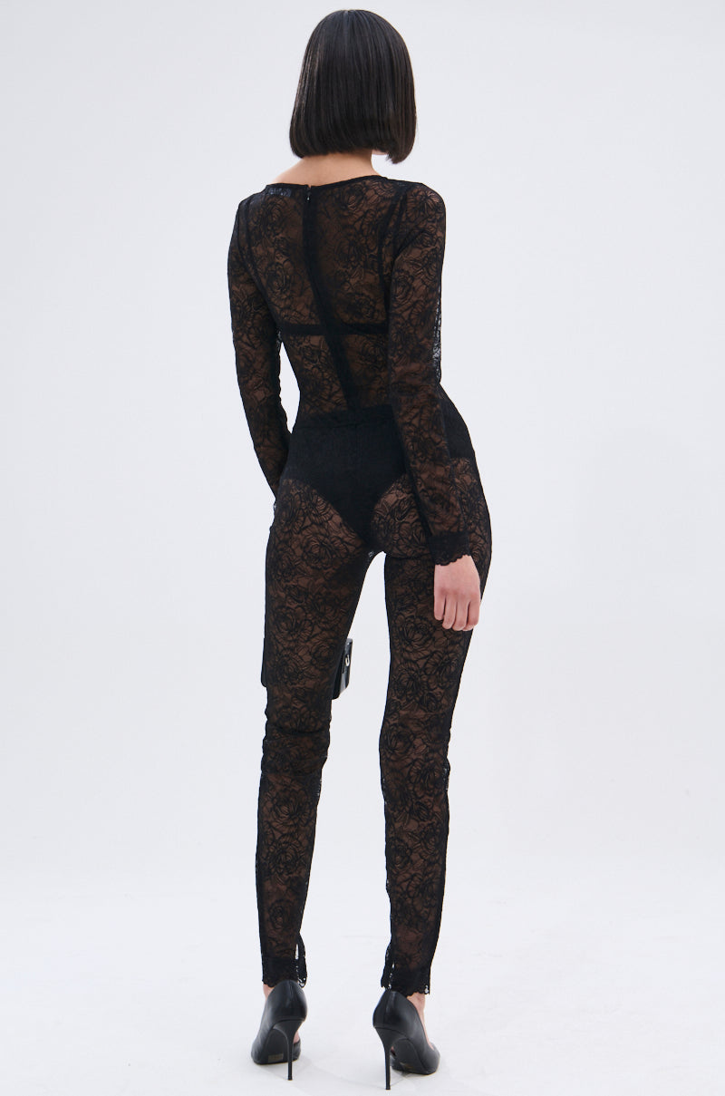 A woman with a sleek bob faces away, wearing the ONLY IF THERE'S BOTTLE SERVICE LACE JUMPSUIT—curve-hugging with sheer floral lace details—and black heels, set against a plain light background.