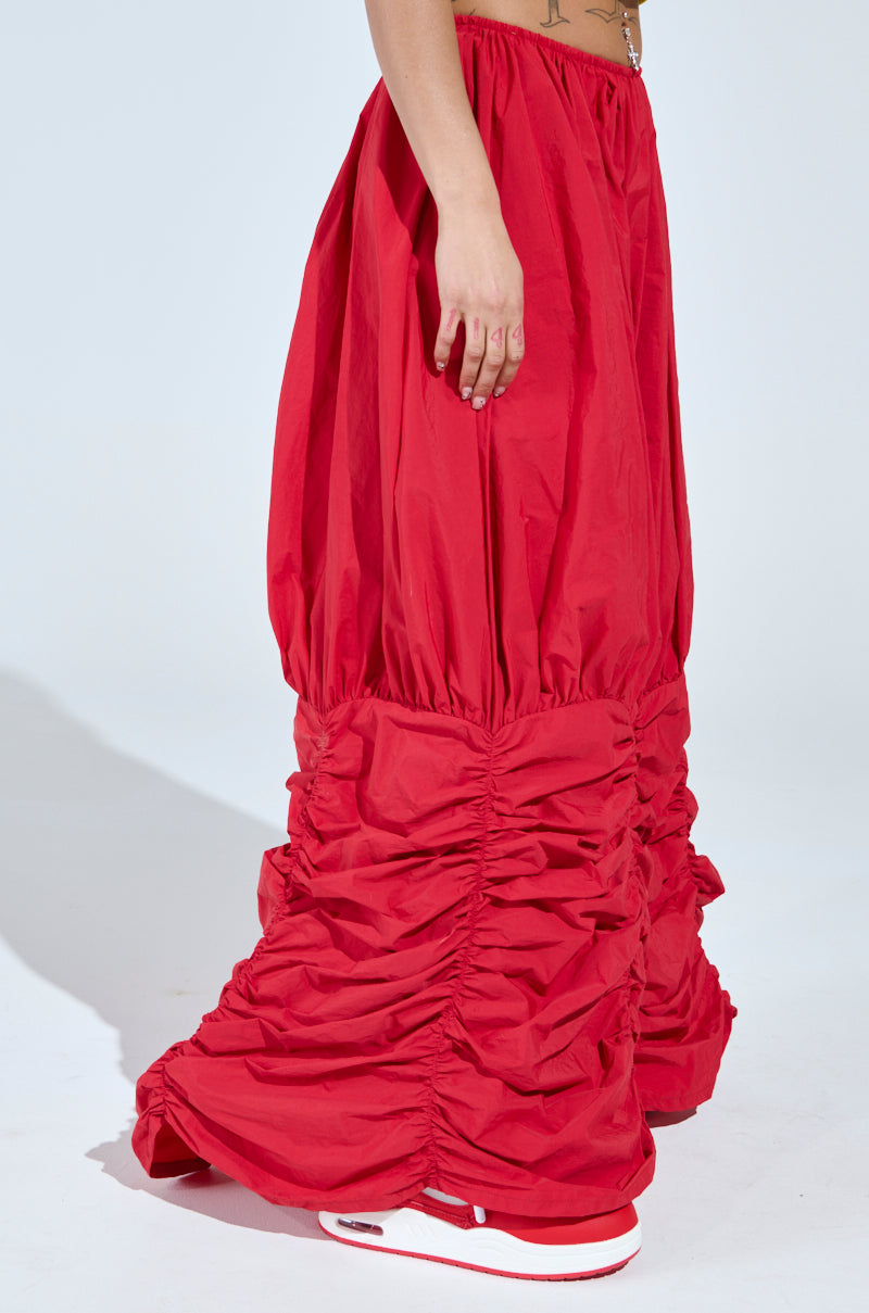 A person models the WIDE LEG SCRUNCHED HEM PANTS in red, featuring a gathered, ruched lower half and paired with white and red sneakers. Only their lower torso and legs are shown against a plain background.