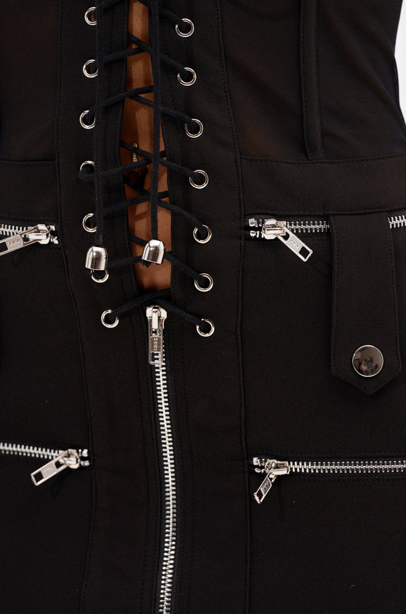 Close-up of the "A LITTLE BIT OF BUSINESS BLAZER DRESS," a structured black blazer dress with silver zippers, corset-style lace-up details with metal eyelets, decorative stitching, and a buttoned flap on one side.