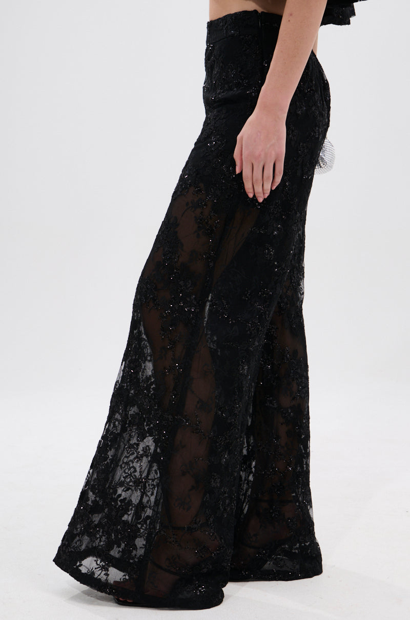Model wears the QUEEN B LACE TROUSER—high-rise, wide-leg trousers in sheer floral mesh with decorative patterns—against a plain white background, showing only the lower torso and legs.