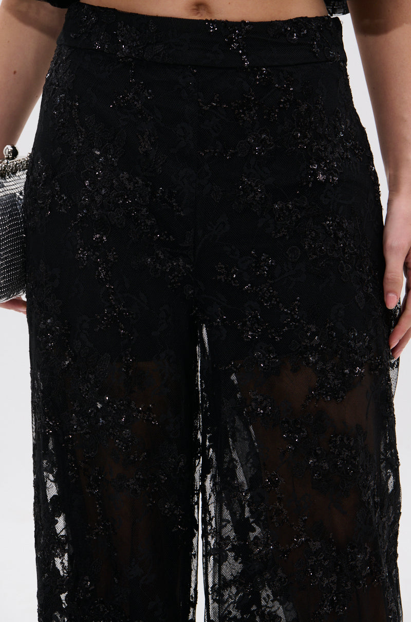 Close-up of a person wearing the QUEEN B LACE TROUSER, showcasing its sheer floral mesh and sequin details, holding a sparkly clutch. Only the lower torso and upper legs are visible.
