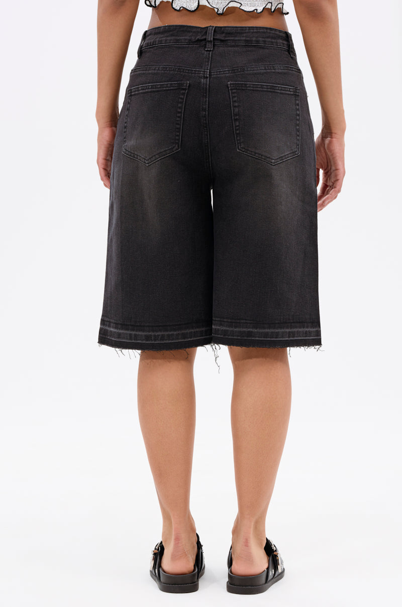 A person stands facing away, wearing the STARS SHINING RHINESTONE BERMUDA SHORT—high-waisted with frayed hems and back pockets—paired with black sandals. Only the lower back and legs are visible against a plain white background.