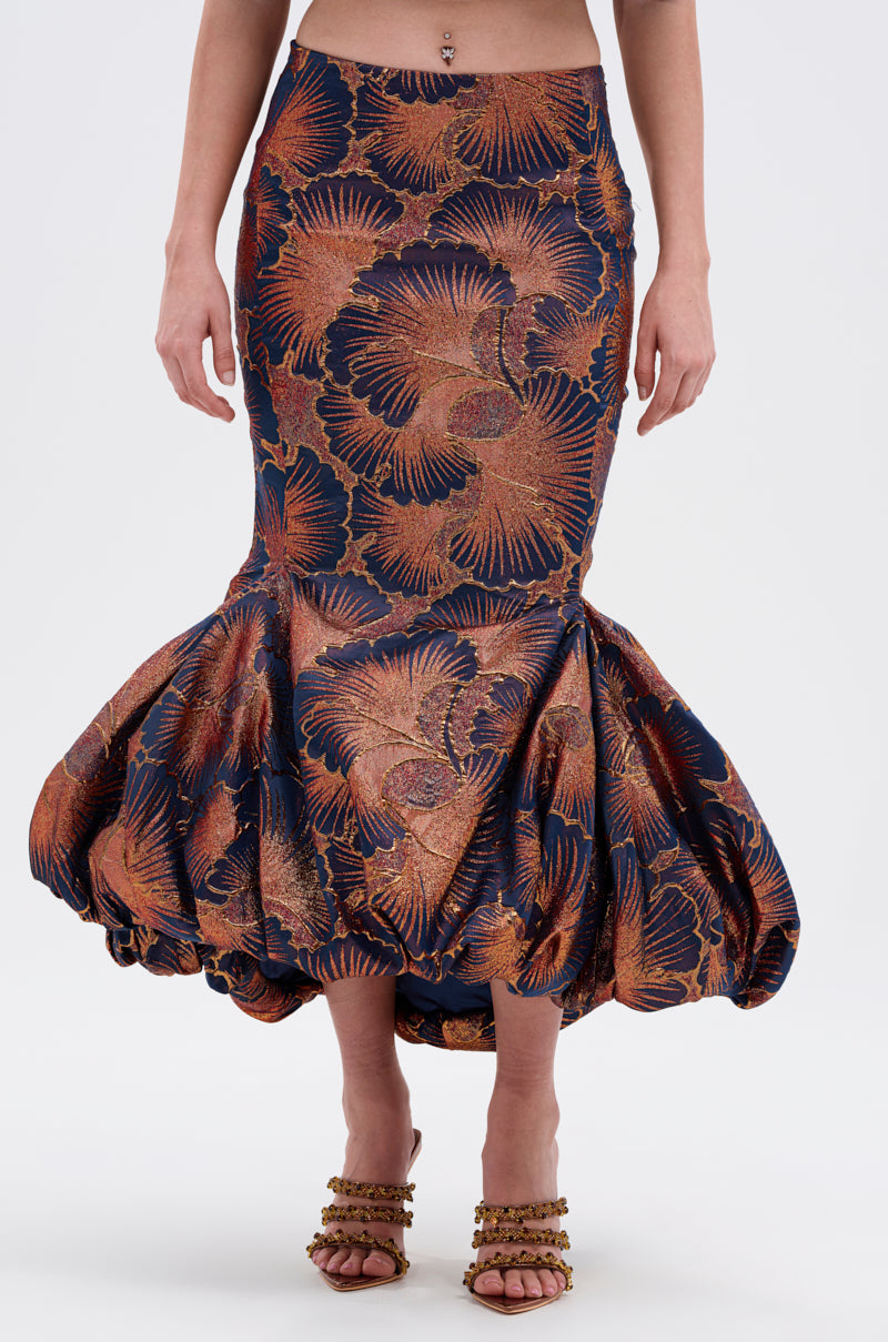 Wearing the LADY LUX BROCADE BUBBLE HEM MIDI SKIRT with a high-rise bubble hem, bold leaf pattern, and adjustable lace-up back, styled with decorative heeled sandals. Image is cropped at the midriff and ankles.