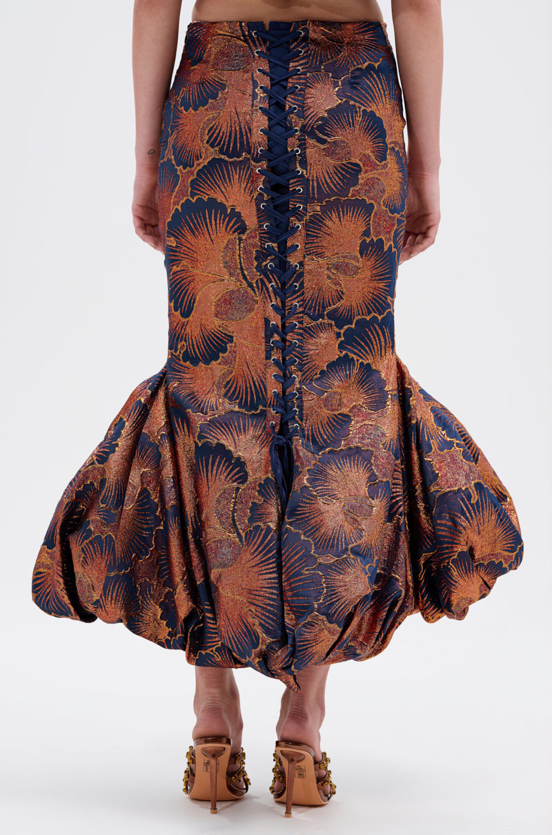 Wearing the LADY LUX BROCADE BUBBLE HEM MIDI SKIRT, a high-rise fitted style with an adjustable lace-up back, showcases a blue and copper floral pattern from waist to legs.