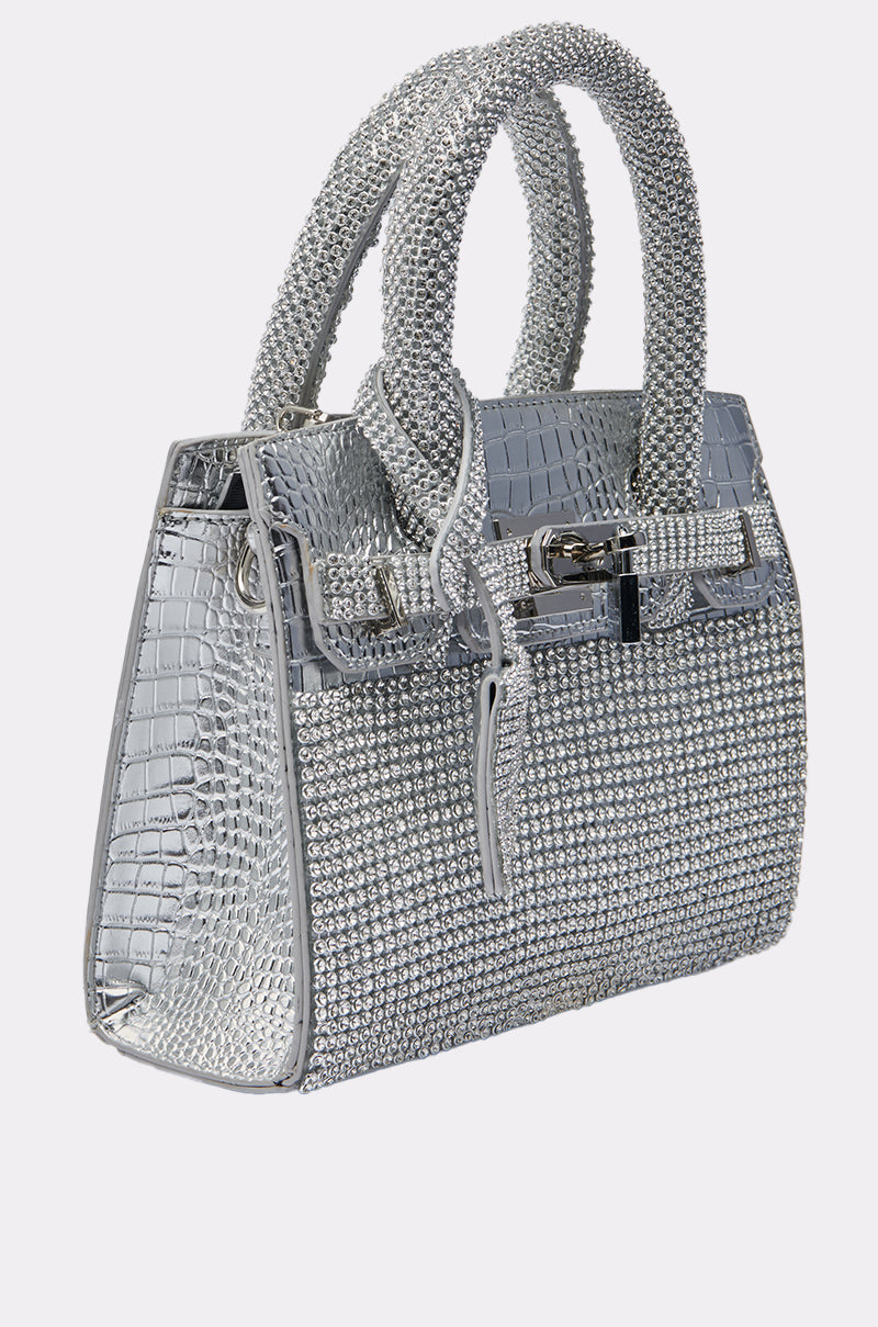 The SWERVE BLING PURSE is a silver crocodile-patterned handbag, fully covered in sparkling rhinestones. It features two rhinestone-encrusted handles plus a decorative front buckle and zipper for added style.
