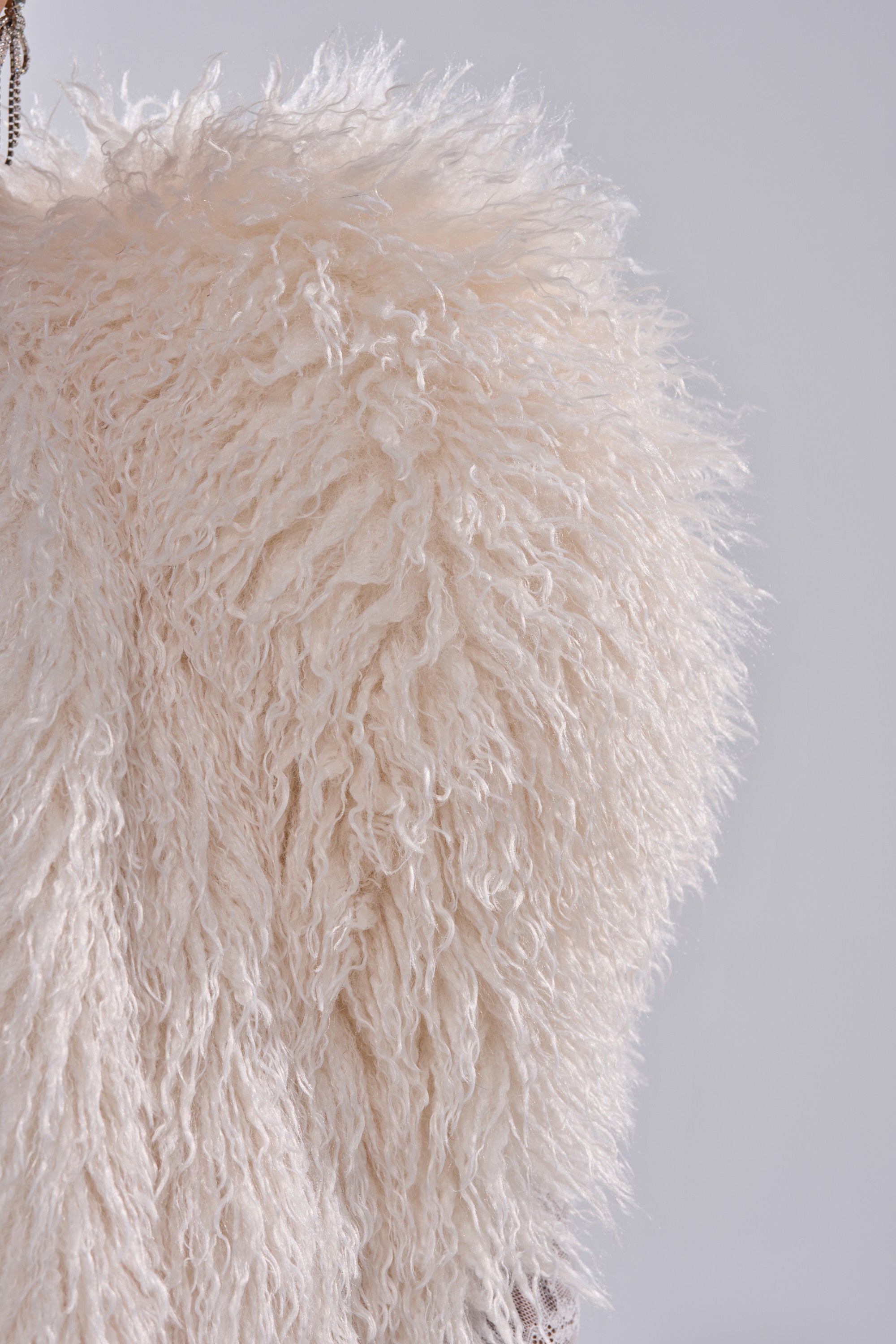 Close-up of the STAR CROSSED LOVER FAUX FUR VEST IN IVORY shows its dense, fluffy ivory faux fur texture against a light gray background, highlighting the cozy, soft curly fibers that make this vest an eye-catching statement piece.