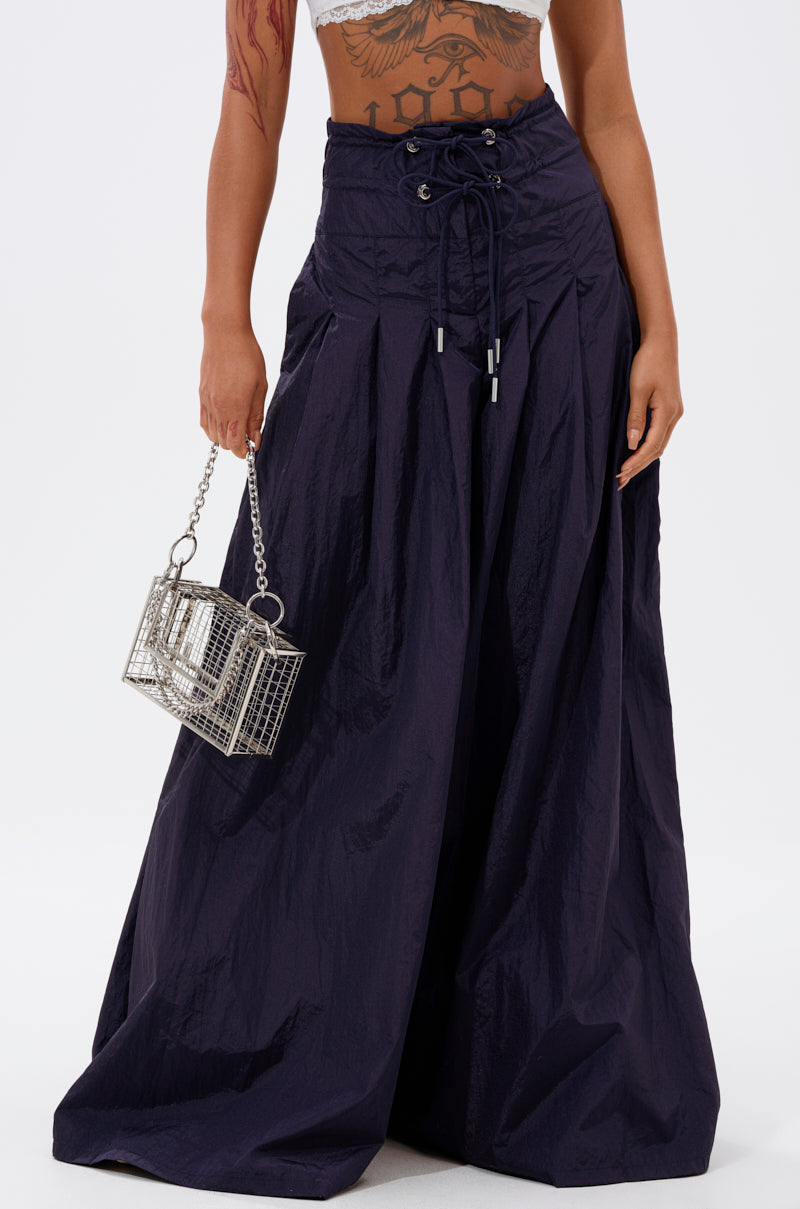 A person wearing the DANCE THE NIGHT AWAY DENIM PALAZZO PANT, which features a wide-leg silhouette and drawstring waist, paired with a white crop top and holding a small silver cage-shaped handbag. Only the lower torso is visible.
