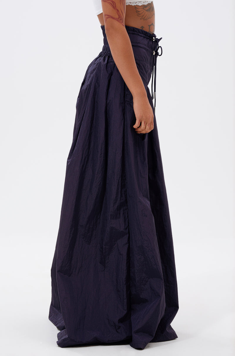 Someone wears the DANCE THE NIGHT AWAY DENIM PALAZZO PANT, a high-waisted, floor-length deep navy pant with a gathered waistband and drawstring, wide-leg silhouette, paired with a white crop top against a plain white background.
