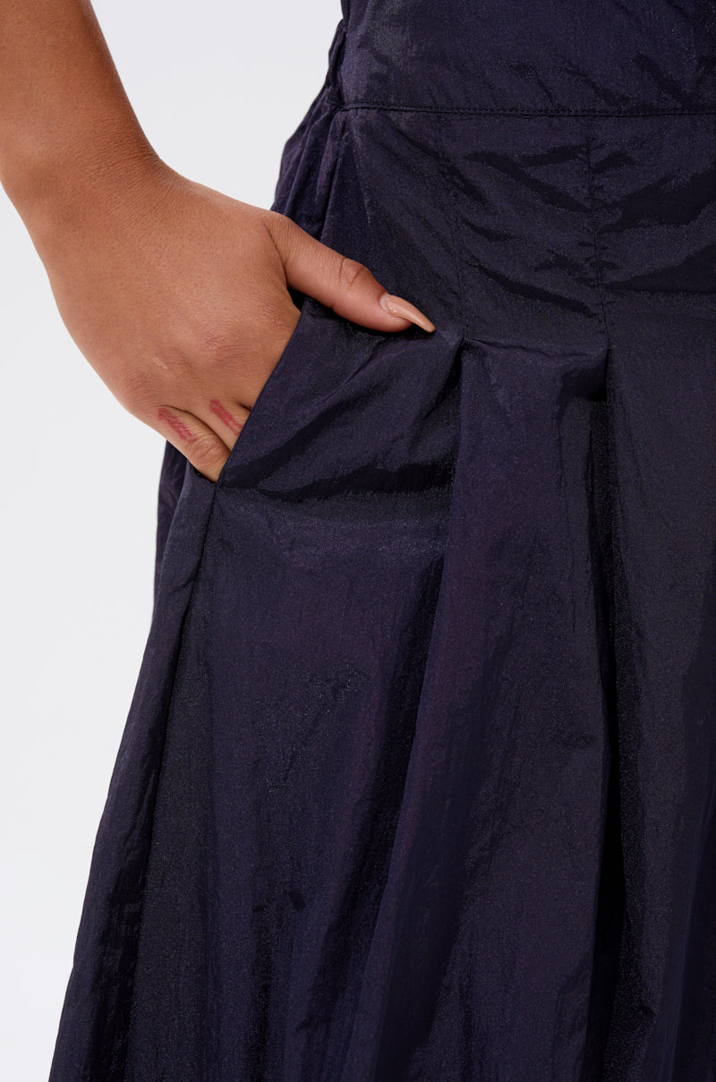 A close-up of a hand resting in the pocket of the DANCE THE NIGHT AWAY DENIM PALAZZO PANT, featuring dark textured denim and a wide-leg silhouette, shown from the waist down against a plain light background.
