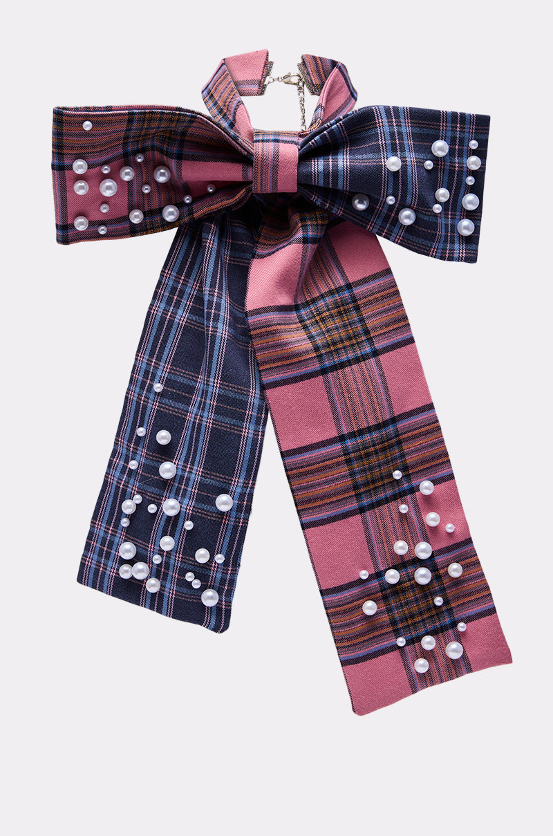 The DREKE OVER THE TOP BOW NECKLACE features a large plaid bow in pink, navy, and white with pearl bead accents, long wide tails, and a metal chain clasp for a chic statement look.