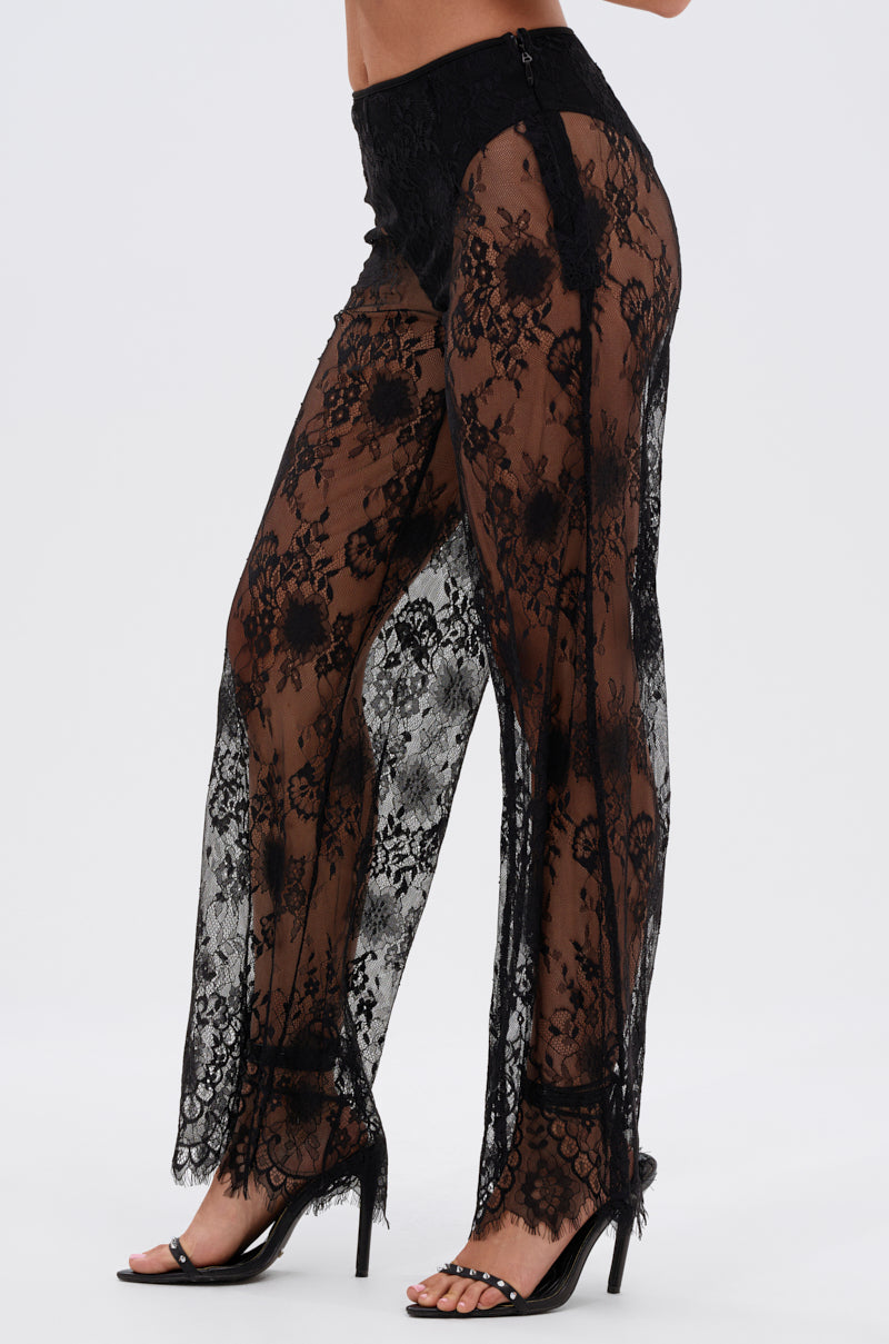 A person wears the DRESSED TO IMPRESS LACE FLARE LEGGING—sheer, floral-patterned, flared leggings revealing black underwear—paired with black high-heeled sandals against a plain white background.