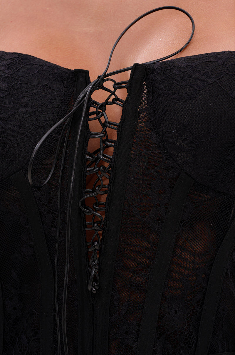Close-up of the DRESSED TO IMPRESS LACE CORSET in black, featuring visible boning, delicate floral lace, and a lace-up center with thin black cords. The strapless top is partially open at the neckline, revealing skin.