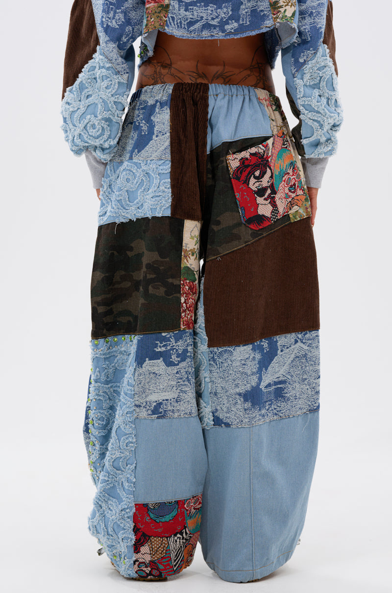 A person models the CALL EM CRAZY PATCHWORK JOGGER—wide-leg jogger pants with denim, corduroy, camo, lace, and colorful fabric patches—standing against a white background for a bold streetwear look.