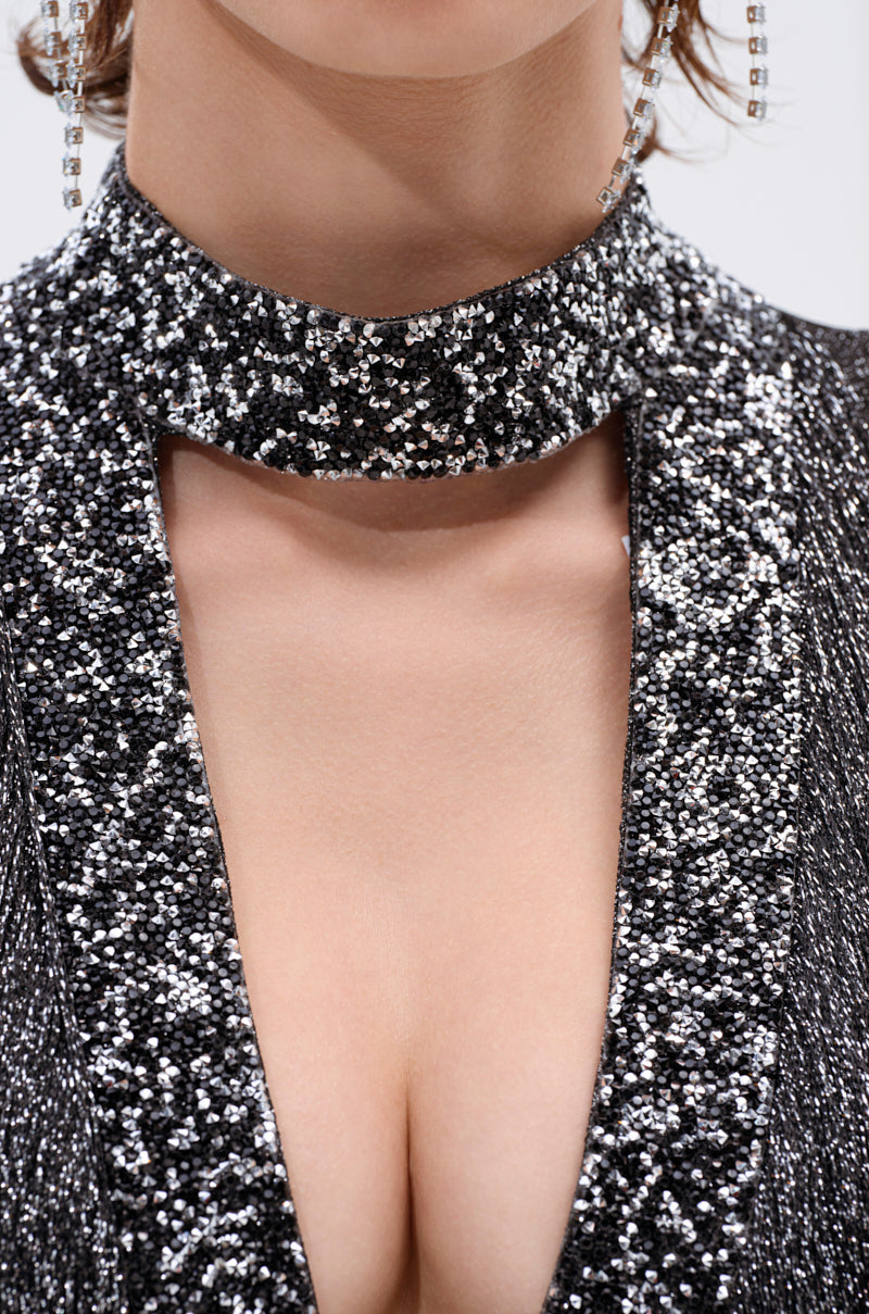 A close-up of a woman wearing the MIXED MESSAGES METALLIC BANDAGE MINI DRESS WITH FRINGE, featuring a high neckline and keyhole cutout. She completes her look with dangling rhinestone earrings.