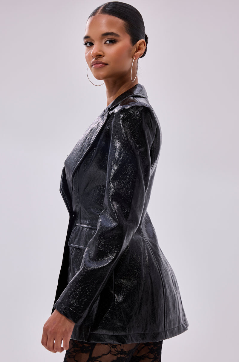 A woman with slicked-back hair and hoop earrings poses confidently against a plain light background, wearing the HERE FOR THE DRAMA PEBBLED BLAZER.