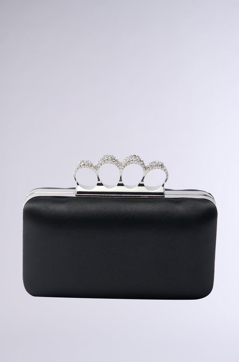 The RING CLUTCH is a rectangular black satin handbag with a silver clasp and four rhinestone-embellished circular rings on top, shown against a plain light gray background.
