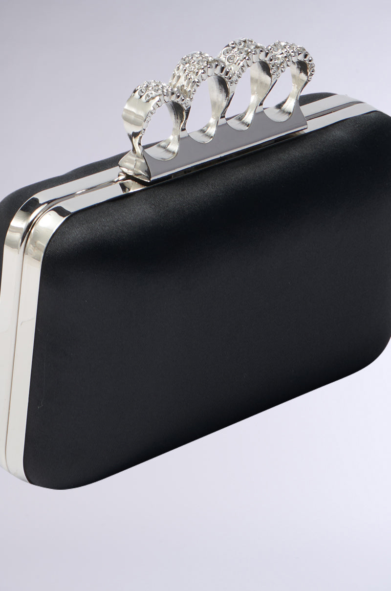 The RING CLUTCH features a black exterior and a silver metallic knuckle handle with rhinestone embellishments, displayed on a light gray background.