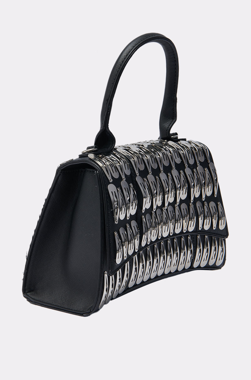 The CLIP IT UP PURSE is a black faux leather mini bag with a single handle, adorned with rows of shiny silver safety pins for a bold, standout look.