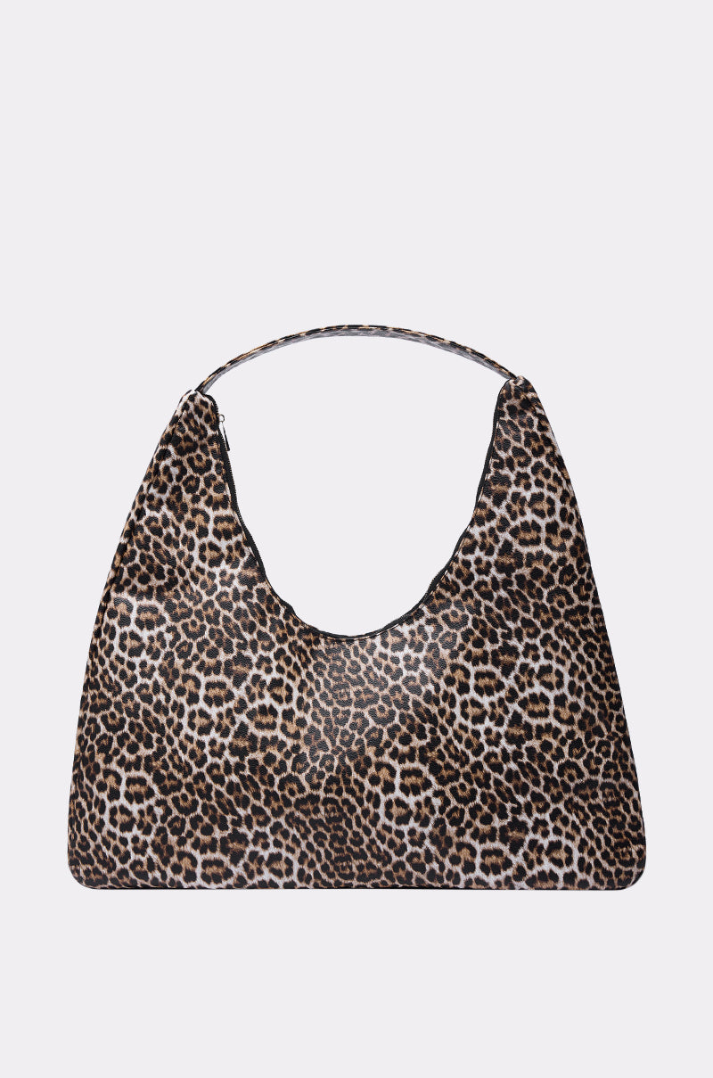 The WILD ONE PU OVERSIZED TOTE is a trapezoid-shaped bag with short handles, showcasing a brown, black, and white leopard print on a plain light gray background.