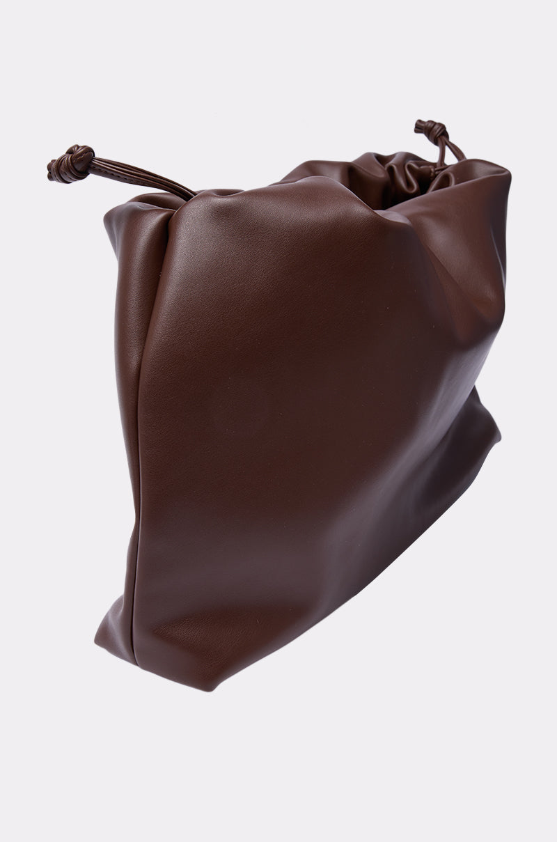 The IN PARIS WITH IT PURSE is a brown, soft faux leather clutch with a smooth texture and knotted drawstring cords, creating a stylish gathered look against a plain light background.