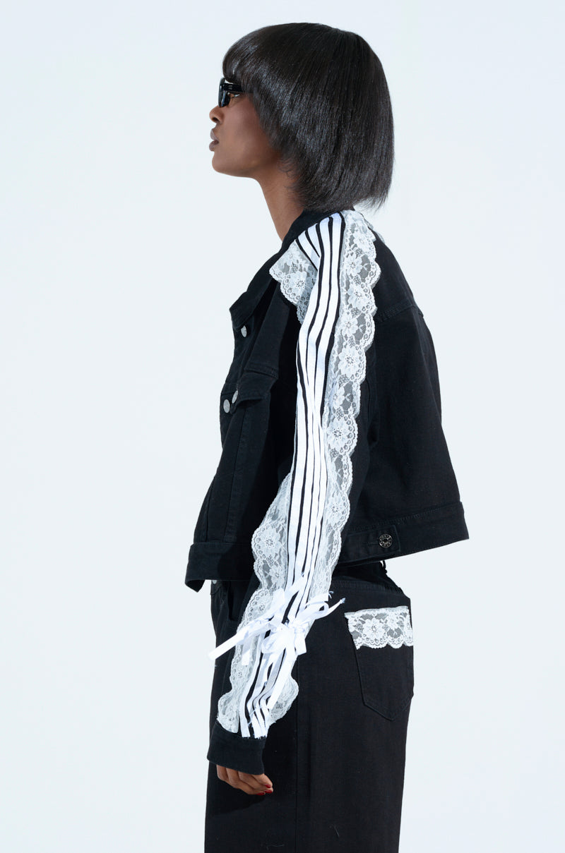 A person in profile with a bob haircut and sunglasses wears the DYLAN LACE DETAIL DENIM JACKET featuring striped details and metallic button cuffs. The dark wash denim jacket is elegantly layered over a white shirt.