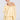 A person models the "ON YOUR MIND CHIFFON MINI DRESS," a pastel yellow, off-the-shoulder dress with ruffled edges and long sleeves, against a white backdrop. The person has blonde hair pulled back and accessorizes with hoop earrings.
