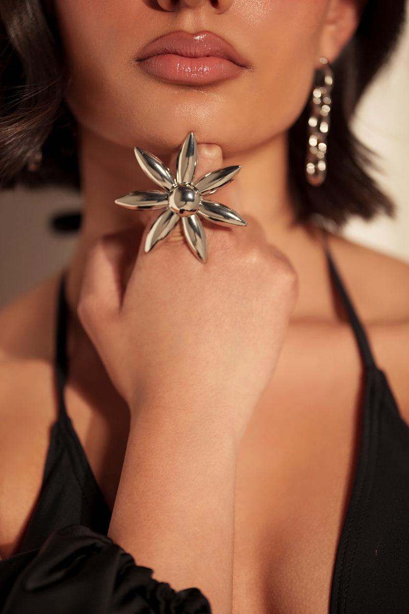 A woman with short, dark hair and chunky silver earrings shows off a large, metallic flower-shaped ring from the IN THE SUN RING SET on her hand, raised to her chin while wearing a black halter top.