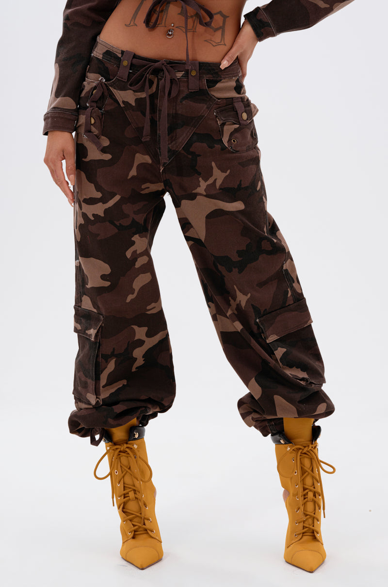 Wearing the CANT SEE ME BROWN CAMP CARGO JOGGER with a tied waistband and wide-leg fit, paired with bright yellow lace-up boots—cropped image shows the lower torso and legs against a plain white background.