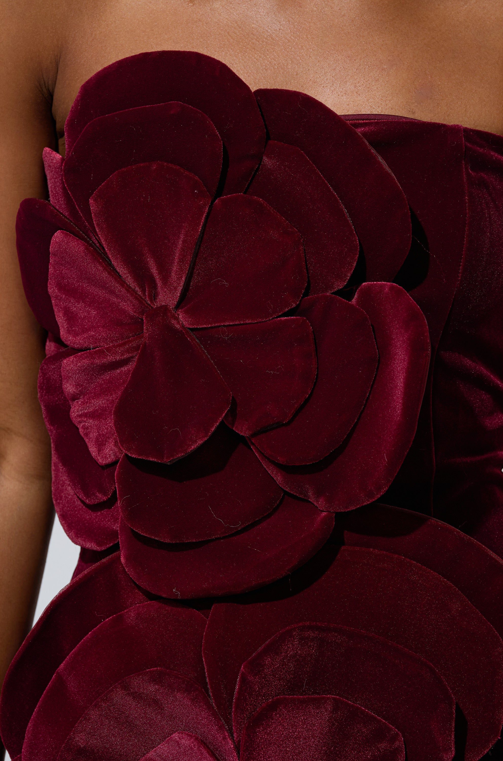 A close-up of a person wearing the FLOWER POWER VELVET MINI DRESS, a strapless deep burgundy mini dress featuring large, layered 3D floral appliqués on the bodice.