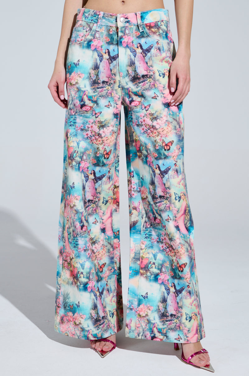 The woman wears Female Fantasy Printed Denim Pants, featuring candy-colored butterflies and figures. Paired with pink pointed heels against a plain light gray backdrop, she radiates whimsical charm.