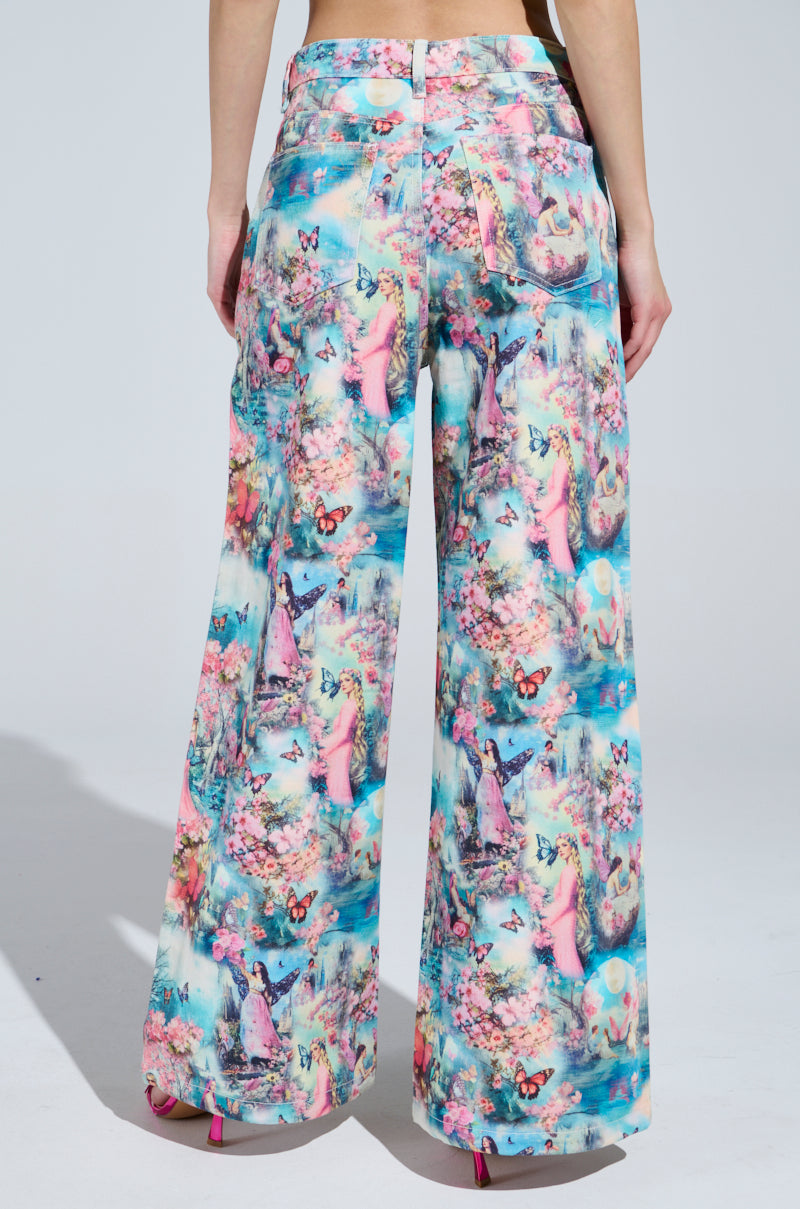 Someone wears vibrant, wide-legged pants with a nature and butterfly candy-colored print. These high-waisted Female Fantasy Printed Denim Pants, paired with pink heels, enchant from the back against a simple gray backdrop.