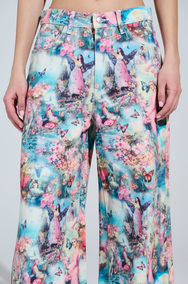 Wearing FEMALE FANTASY PRINTED DENIM PANTS, a person showcases vibrant, candy-colored jeans with a high-rise fit. The intricate design features pink, blue, and green angels, butterflies, and floral motifs. Complete with button closure and visible pockets against a plain gray backdrop.