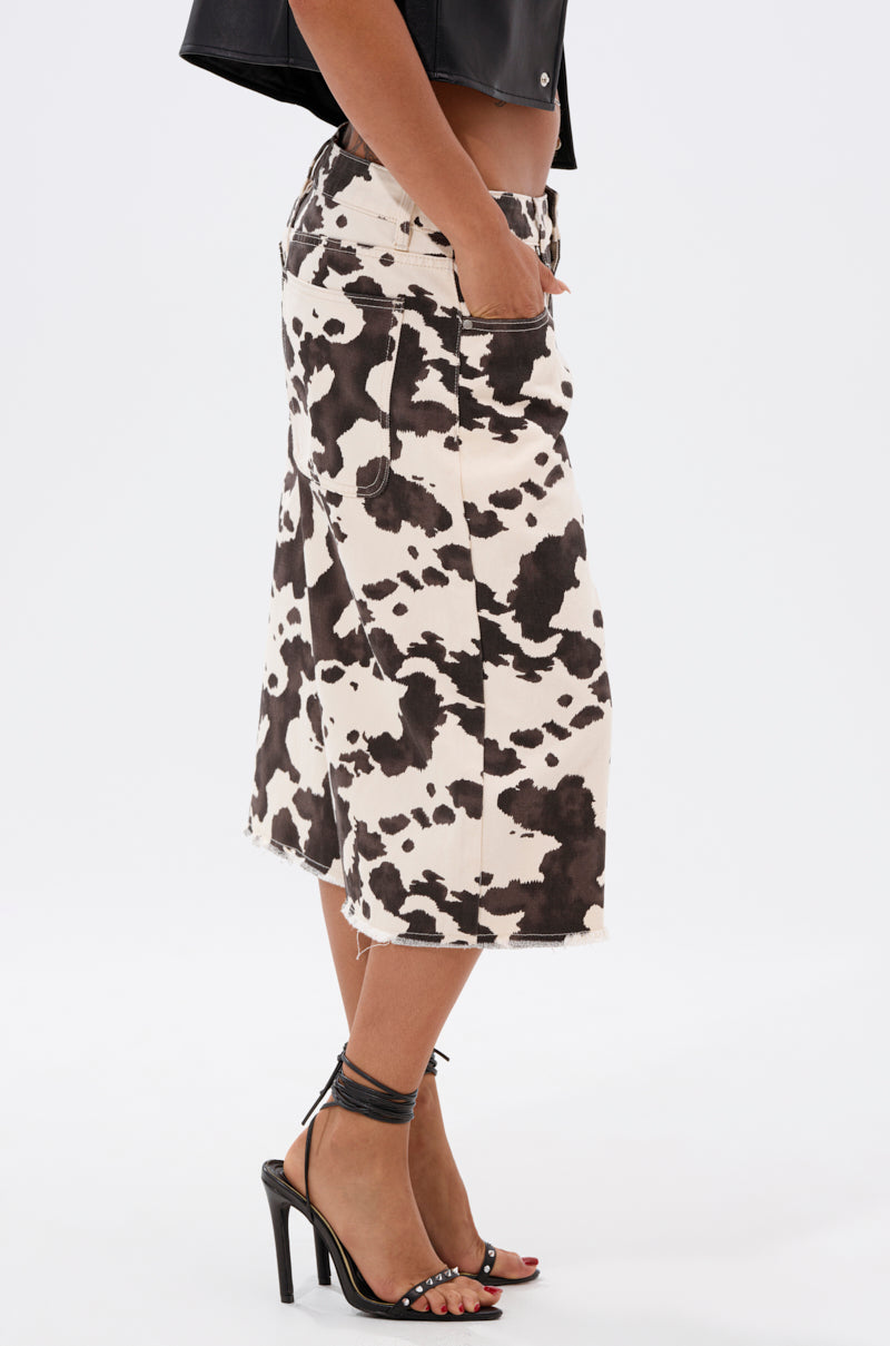 A person stands in profile wearing the COOLEST ON THE BLOCK COW HIDE BERMUDA SHORT, paired with a black cropped jacket and black ankle-strap high-heeled sandals, with one hand in their pocket.