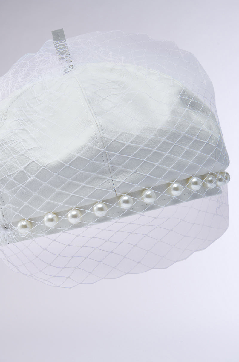 The EDITORIAL BERET is a white cap featuring a tonal mesh veil with a crisscross pattern and pearl-embellished trim. It stands out elegantly against a plain light gray background.