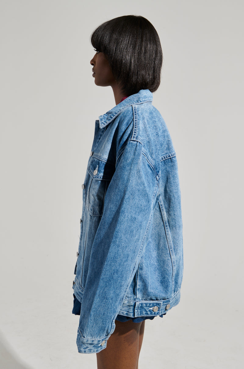 A person with medium-length dark hair is seen in side profile, wearing the GOTTA GO OVERSIZED DENIM JACKET with faux silver hardware against a plain background.
