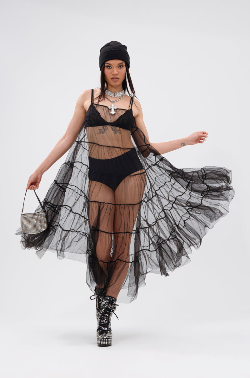 A woman poses in the PERFECT FOR LAYERING TULLE MAXI DRESS over black lingerie, styled with a black beanie, sparkling platform boots, statement necklace, and a small beaded handbag against a plain white background.