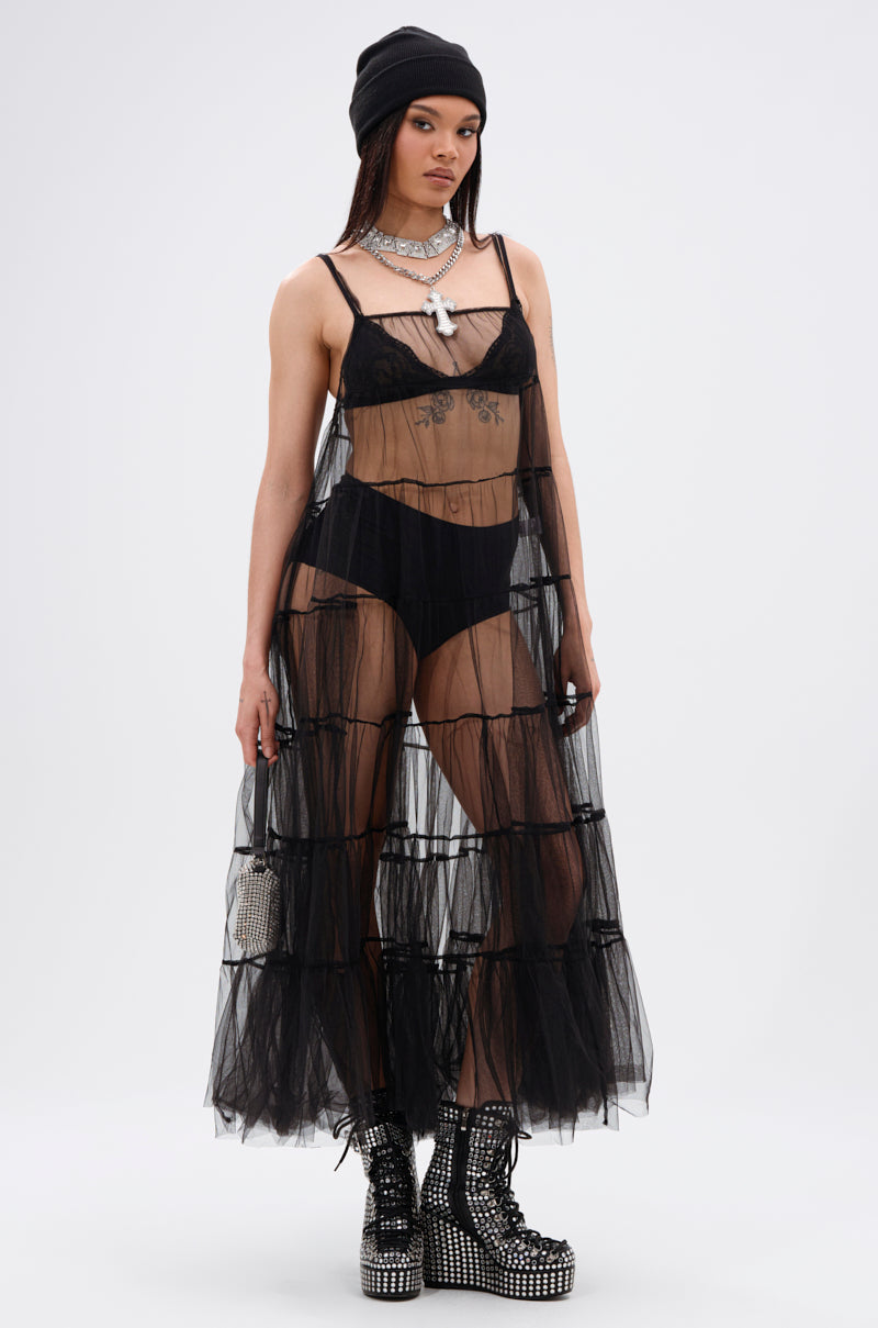 A woman wears the PERFECT FOR LAYERING TULLE MAXI DRESS over black lingerie, styled with a black beanie, layered necklaces, studded platform boots, and a small bag, standing against a plain white background.