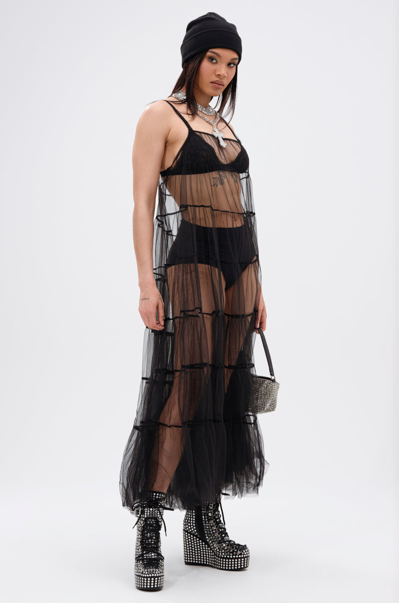 Someone wears the PERFECT FOR LAYERING TULLE MAXI DRESS—a sheer black, ruffled maxi dress—over black underwear, styled with platform studded boots, a black beanie, silver jewelry, and a sparkly handbag, against a white background.